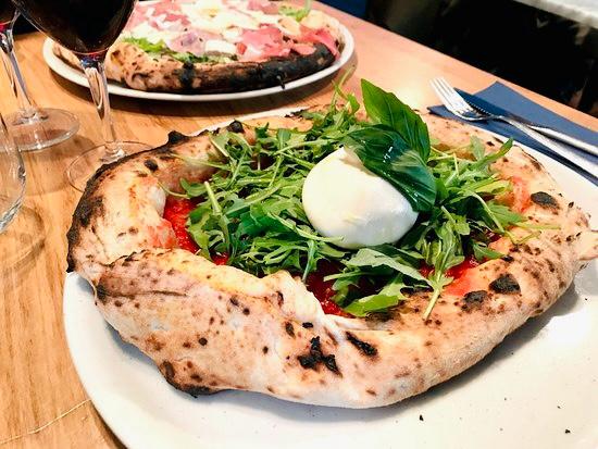 Pizza napolitaine à la burrata, roquette et tomate, posée sur la table en bois de la salle